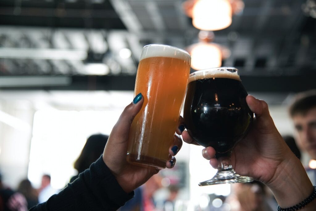 Manos con vaso y copa llena de cerveza, mano derecha cerveza oscura y mano izquierda cerveza clara.