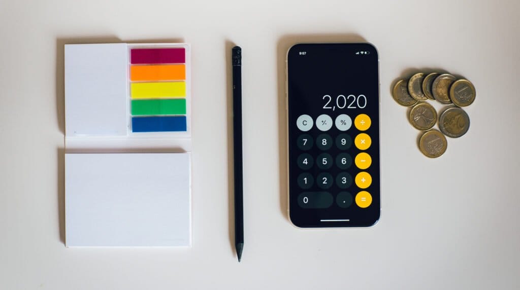 post its de colores, un bolígrafo, una calculadora con la cifra "2,020" y unas monedas en el costado derecho