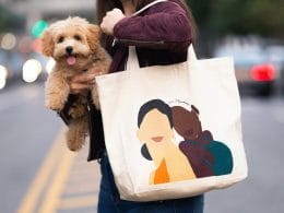mujer sostiene a perro color cafe con el brazo derecho y una bolsa de tela cuelga de su hombro izquierdo