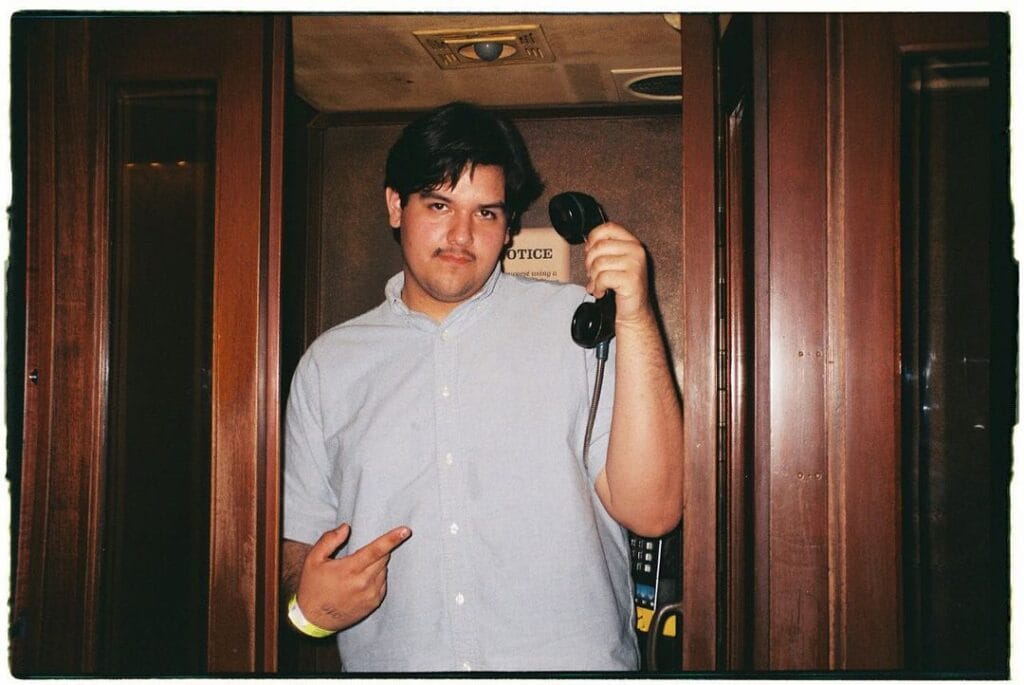 Hermosillo. Chico con camisa de botones color gris claro. En la mano izquierda tiene un teléfono publico de color negro.