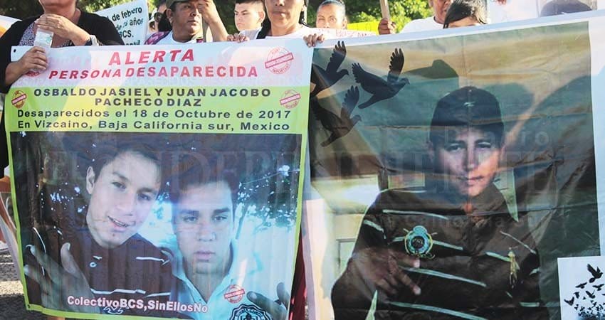 Personas sostienen mantas con foto de personas desaparecidas en Baja California Sur. DEsapariciones en México.