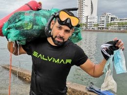 Hombre con visores y esnorquel carga bultos con basura salida del mar