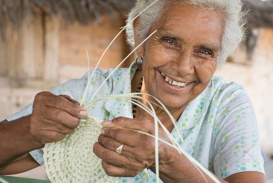 Mujer mayor sonriendo y elaborando trabajo de cestería. 