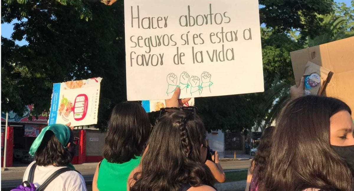 Manifestación en Hermosillo durante 2021, por el derecho a decidir. En la imagen se ven cuatro mujeres de espaldas quienes elevan sus carteles. Uno de ellos dice «Hacer abortos seguros sí es estar a favor de la vida».