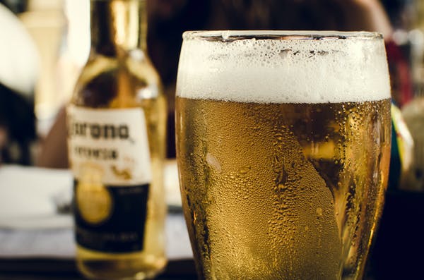Una vaso de cerveza lleno y sudado, de fondo una botella de cerveza.