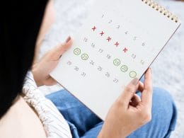 Una mujer revisa un calendario marcado con equis rojas y círculos verdes.