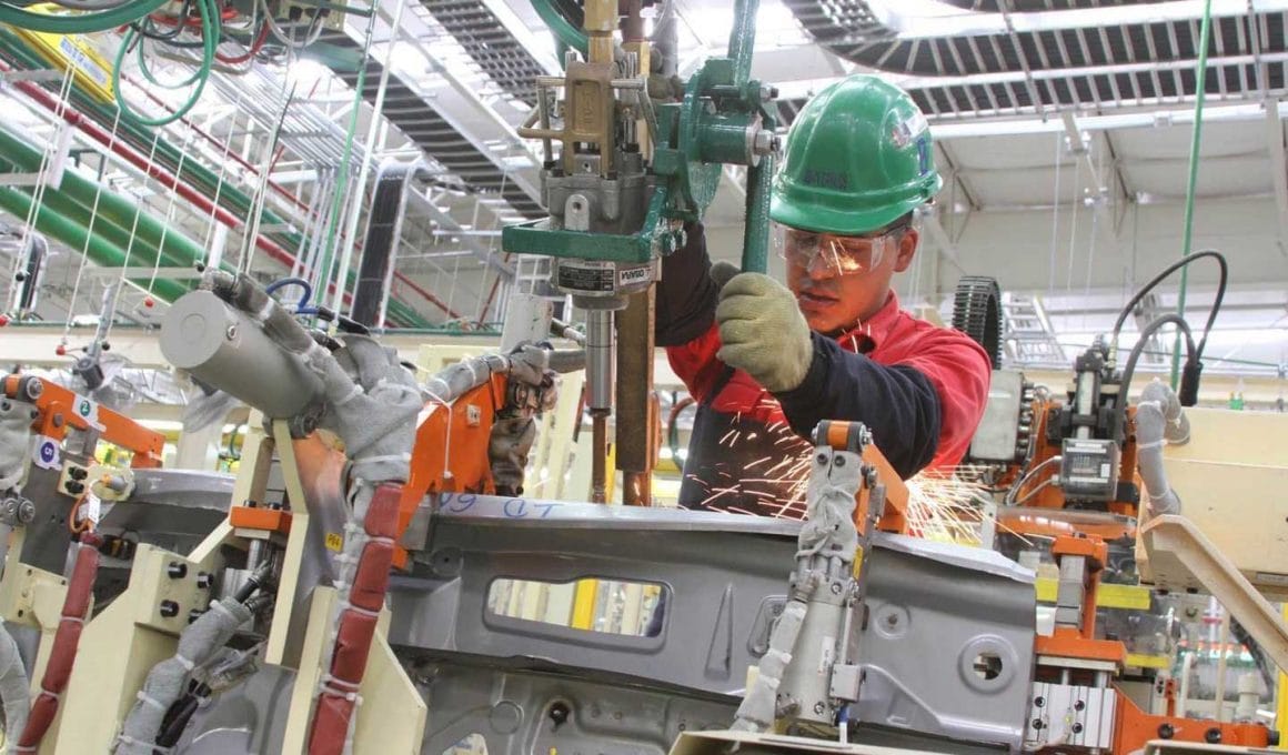 Un hombre trabaja en una maquinaria industrial. Porta casco verde.