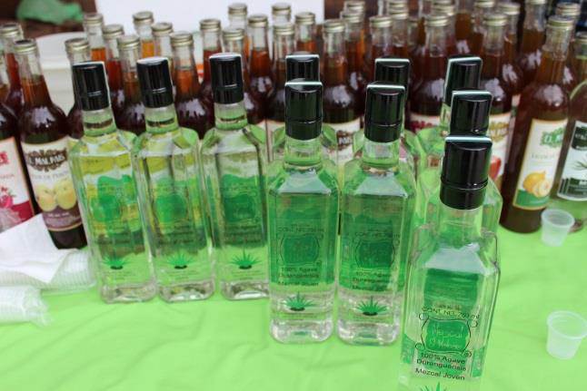 botellas de cristal con mezcal alineadas sobre mesa con mantel verde